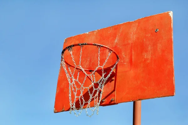 Closeup of red basketball hoop in playground. Rusty old outdoor basketball red board, closeup. Basketball hoop with blue sky background.