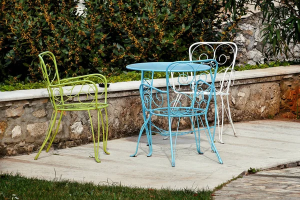 Chaises et une table dans le jardin. Chaises en acier colorées et une table debout dans un beau jardin au soleil. Meubles de patio. Un ensemble de trois chaises colorées et une petite table ensemble extérieur . — Photo