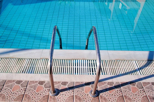 Handrail on the pool. Swimming pool with stair closeup. Pool handrails view. Water swimming pool with sunny reflections. Steel handrail, swimming, summer, travel. The entry to the pool with handrail. — Stock Photo, Image