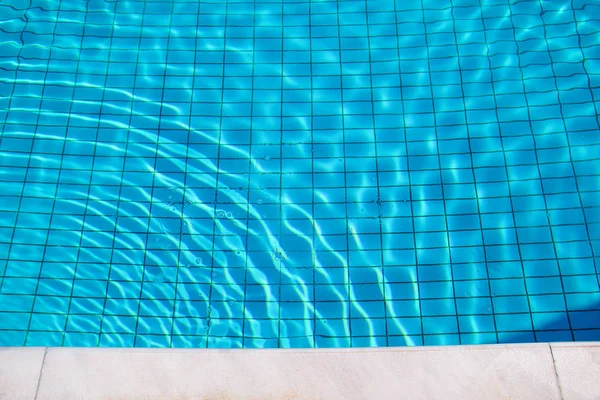 Blue ripped water in swimming pool. Swimming pool bottom caustics ripple and flow with waves background. Clear light blue pool water ripples with sun reflections. Surface of blue swimming pool. — Stock Photo, Image