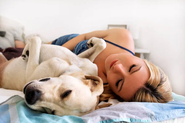 Woman with dogs at home. Handsome woman resting and sleeping with her dog in bed in the bedroom. Owner and dog sleeping. Pet concept. Yellow labrador retriever relax, lonely woman and her best friend.