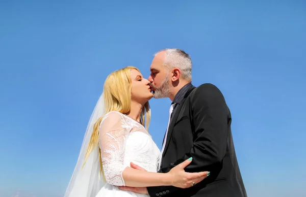 Concepto de boda. La pareja de novios guapos felices están de pie y besándose. novio romántico y novia en el amor abrazo. En el fondo es hermoso entorno natural de cielo azul. Felicidad . —  Fotos de Stock