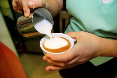 Barista onun kahve dükkanı veya kafe kapuçino yapma. Beyaz kahve fincan içine bir kahve latte sanat yapmak Barista dökme latte köpük. El sütü bir kaseye kahve tam dökülen. Sıcak bir içecek.