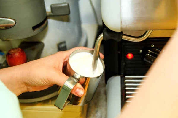 Women make foaming milk in a coffee machine in bar. Closeup of Caucasian woman barista hands holding milk jug for making coffee using coffee machine. A female hand milking milk in a coffee maker.