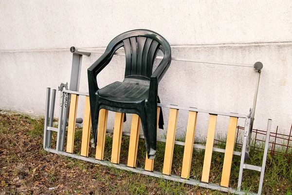 Zelená zahradní plastové židle vyhodil a nechal na žebříku ke zdi v zahradě. Zeď na pozadí, příroda, židle nábytek. Recyklační průmysl, ochrana životního prostředí. recyklovaný materiál, odpady. — Stock fotografie