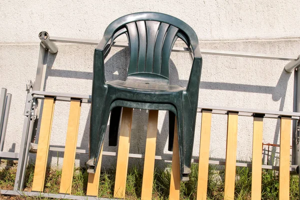 Grön plast trädgårdsstolar kastas bort och kvar på en stege av väggen i trädgården. Vägg bakgrund, natur, stol möbler. Återvinningsindustrin, miljöskydd. återvunnet material, avfall. — Stockfoto