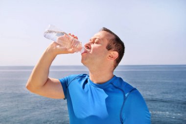 Sporcu eğitim sırasında bir mola verme taze temiz su bir Şişeden içme aittir ve arka plan bir güzel manzara doğa dışarıda ormanda ile temiz hava sahiptir. Sağlıklı yaşam tarzı.