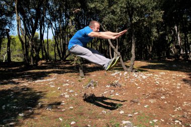 Kaslı adam ormandaki hava egzersiz egzersiz atlama yapıyor. Yakışıklı sporcu spor giyim giymek kadar açık havada doğa manzara hava alýþtýrmasýnda atlıyor. Uygun, sağlıklı yaşam konsepti çapraz.
