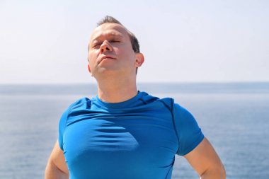 Athletic sabah egzersiz için bir sahil hazırlanıyor germe egzersiz yaparak yerleştirmek. Rutin güneşin altında uzanan bir boyun yapıyor yakışıklı fitness atlet. Mavi gökyüzü ve denizin içinde geçmiş.