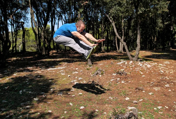 Man doing workout jump up in air exercise in forest. Handsome sportsman wearing sportswear is jumping up in air exercise in beautiful landscape nature outdoors. Cross fit, healthy lifestyle concept.