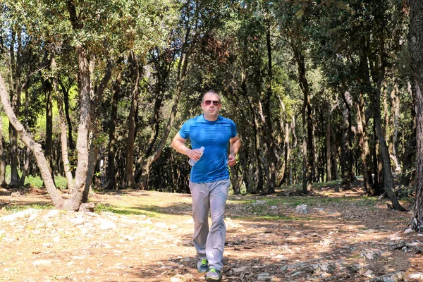 Running man jogging for fitness running in beautiful landscape nature outdoors. Handsome young spotrsman wearing sportswear and running and exercises in forest, in the natural environment, sunny day.