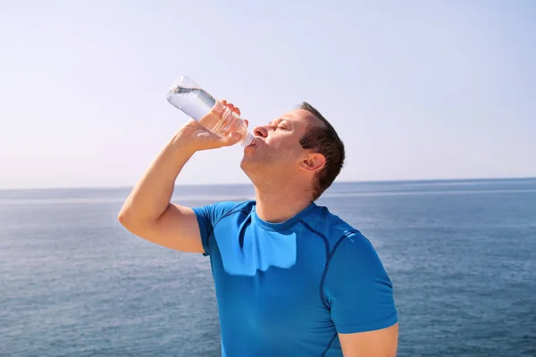 An athlete making a break during training, drinking fresh clean water from a bottle, rests and enjoys the clean air, with a beautiful landscape nature outdoors forest in background. Healthy lifestyle. — Stock Photo, Image