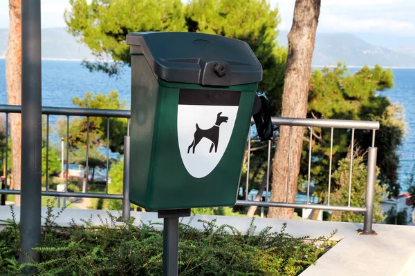 Green dog waste container in a tourist complex near the sea / Public trash can for dog waste poop sign / Garbage container of dog pet garbage / Pet Waste bin Stations. Vertical view, outdoor.