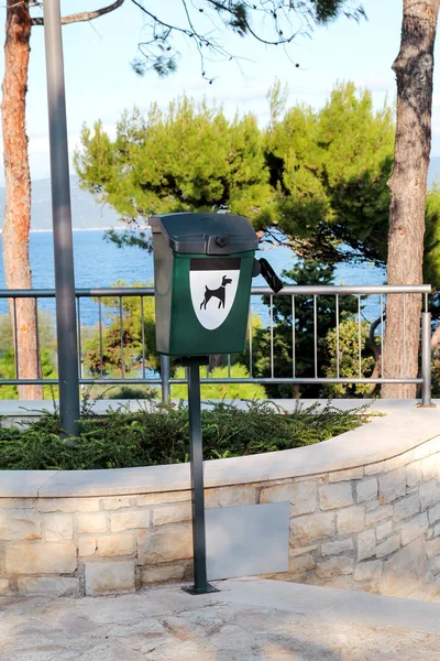Green dog waste container in a tourist complex near the sea / Public trash can for dog waste poop sign / Garbage container of dog pet garbage / Pet Waste bin Stations. Vertical view, outdoor.