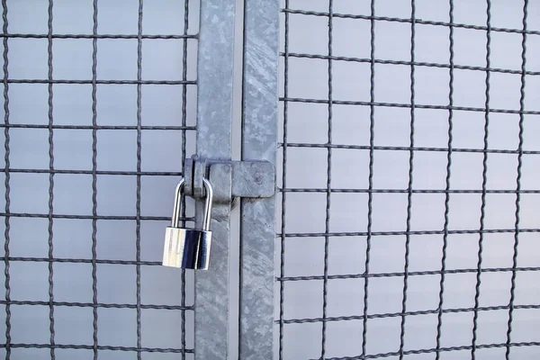 Padlock on a chainlink fence / Master key and old rusty chain with steel cage, close up / Closed lock with a chain on an old metal fence / Metallic locks to fence gate.