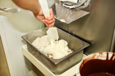 Kadın işçi Ice cream maker makina üzerinde çalışıyor. Vanilyalı dondurma ile çikolata sosu ve o üreten çelik konteyner içine düşüyor. Kremalı dondurma endüstriyel hazırlanması. Tatlı, tatlılar.