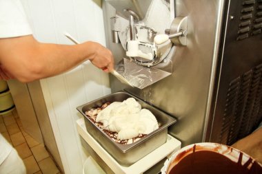 Kadın işçi Ice cream maker makina üzerinde çalışıyor. Vanilyalı dondurma ile çikolata sosu ve o üreten çelik konteyner içine düşüyor. Kremalı dondurma endüstriyel hazırlanması. Tatlı, tatlılar.
