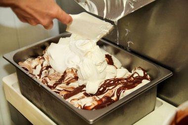 Kadın işçi Ice cream maker makina üzerinde çalışıyor. Vanilyalı dondurma ile çikolata sosu ve o üreten çelik konteyner içine düşüyor. Kremalı dondurma endüstriyel hazırlanması. Tatlı, tatlılar.