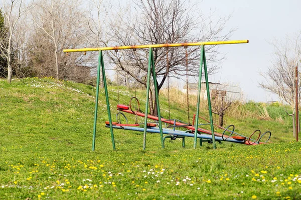 子供のスイングを空にして公共の公園での遊び場活動をシーソー 美しい自然環境 春の花 カラフルな子供のための運動場装置 日当たりの良い春の日 — ストック写真