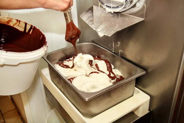 Woman working at ice cream factory is decorations of creamy vanilla ice cream with chocolate dressing in steel container. Pouring chocolate in the tray with frozen ice cream. Beautiful dessert, sweet.