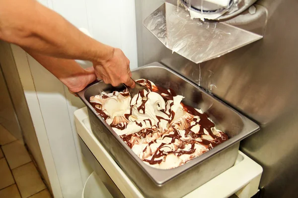 Woman working at ice cream factory is decorations of creamy vanilla ice cream with chocolate dressing in steel container. Pouring chocolate in the tray with frozen ice cream. Beautiful dessert, sweet.