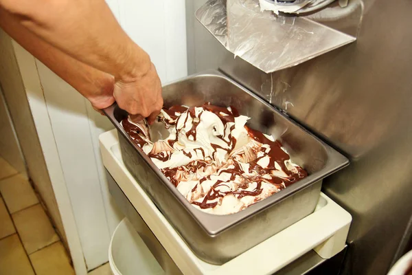 Woman working at ice cream factory is decorations of creamy vanilla ice cream with chocolate dressing in steel container. Pouring chocolate in the tray with frozen ice cream. Beautiful dessert, sweet.