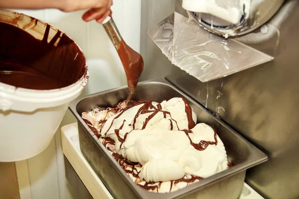 Woman working at ice cream factory is decorations of creamy vanilla ice cream with chocolate dressing in steel container. Pouring chocolate in the tray with frozen ice cream. Beautiful dessert, sweet.