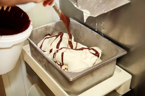 Woman working at ice cream factory is decorations of creamy vanilla ice cream with chocolate dressing in steel container. Pouring chocolate in the tray with frozen ice cream. Beautiful dessert, sweet.