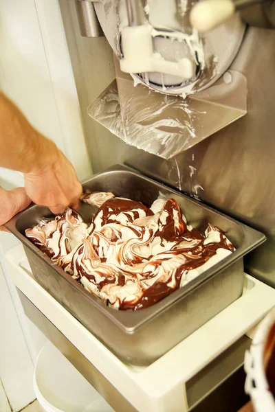 Woman working at ice cream factory is decorations of creamy vanilla ice cream with chocolate dressing in steel container. Pouring chocolate in the tray with frozen ice cream. Beautiful dessert, sweet.