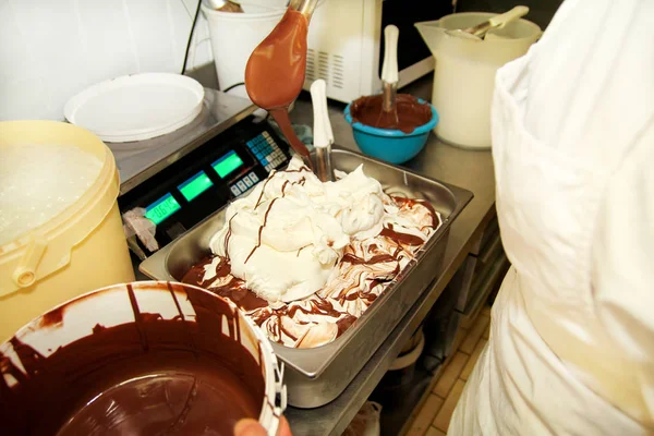 Woman working at ice cream factory is decorations of creamy vanilla ice cream with chocolate dressing in steel container. Pouring chocolate in the tray with frozen ice cream. Beautiful dessert, sweet.