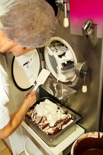 Female chef and worker is working at ice cream factory is cleaning ice cream maker machine from the ice cream leavings. Preparation of ice cream.