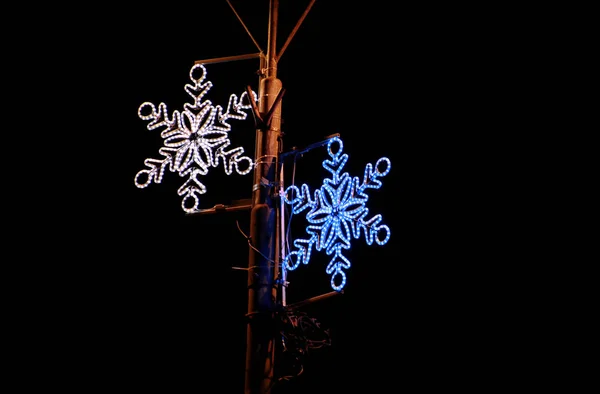 Christmas blue and white lights simulating shape of frozen snowflakes. Street detail of New Year and Christmas decorations, string rice lights bulbs. Ornaments to christmas celebration, holiday scene. Royalty Free Stock Images