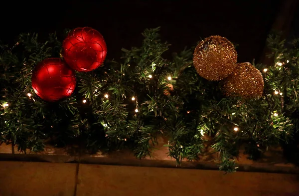 Boules de Noël décorées traditionnelles sur une couronne faite de branches de sapin vert ou d'épinette et de guirlandes éclatantes à l'extérieur. Boules de Noël en pin, rouge et or comme décoration pour les fêtes de fin d'année . — Photo