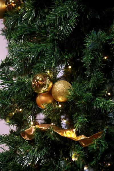 Traditional decorated baubles hangs on green twigs tree of pine. Bright gold balls on Christmas tree of fir or spruce with string rice lights bulbs. Ornaments to christmas celebration, holiday scene. Stock Picture