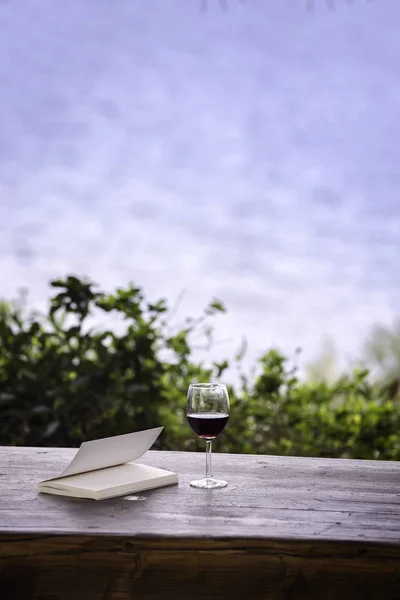 Kırmızı şarap bardağı ve güneş patlaması ahşap masa üzerinde eski açık kitap. vintage filtreli görüntü