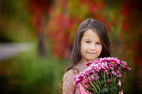 Retrato de menina adorável com um buquê de crisântemos em um fundo de folhagem de outono colorido — Fotografia de Stock