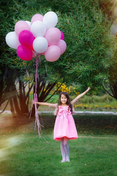 Menina encantadora em um carrinho de vestido rosa inteligente com um grande grupo de balões rosa . — Fotografia de Stock