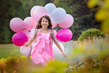 Pembe balonlar büyük bir grup ile karşılamak için akıllı pembe elbiseli çekici küçük kız gider. Seçici odak.