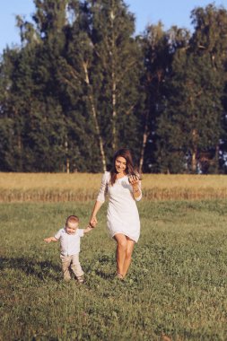 Beyaz elbiseli çekici genç anne el genç oğlun yaz alanına yürüyor. Yatay fotoğraf