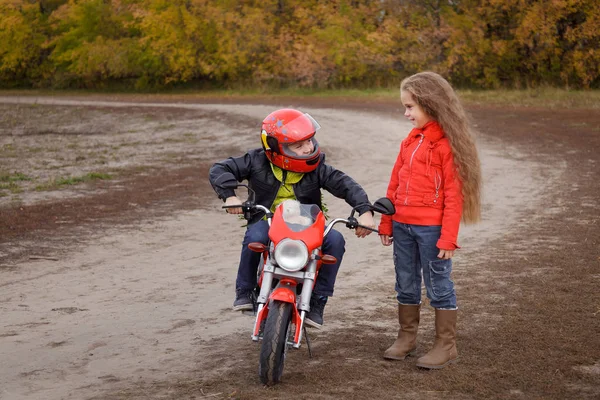 A little boy came on a date to his beautiful girlfriend on a toy motorcycle. Romance on the autumn forest road.