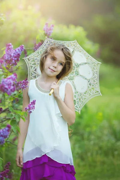 Romántica joven hermosa chica en un vestido blanco con paraguas de encaje se encuentra en el jardín de primavera lila — Foto de Stock