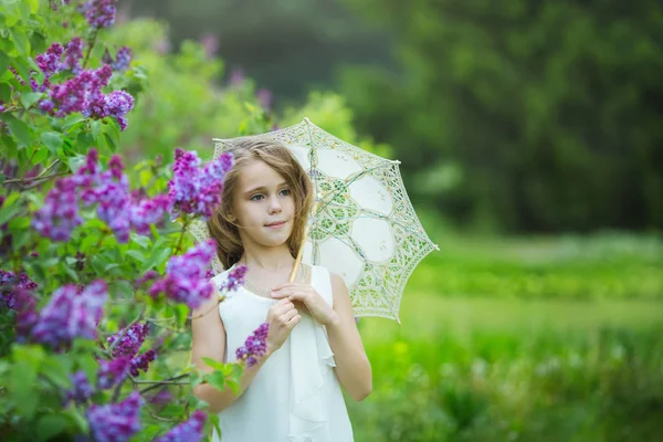 Romántico retrato primaveral de joven hermosa chica en un vestido blanco con paraguas de encaje en flores lila — Foto de Stock