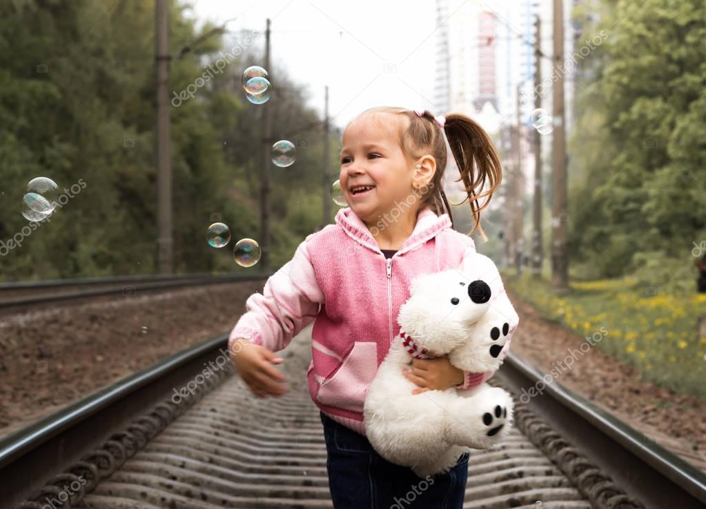 A lonely girl with teddy bear on railway