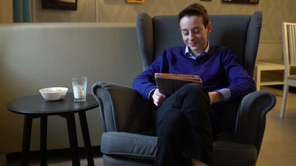 Genç bir sandalyede oturuyor ve bir tablet okuma — Stok video