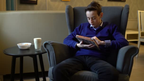 Teen using tablet sitting in a chair and drinking coffee — Stock Video