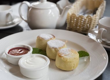 Bir tabak peynirli kek krem sos ve bir kahvaltı masasında reçel ile