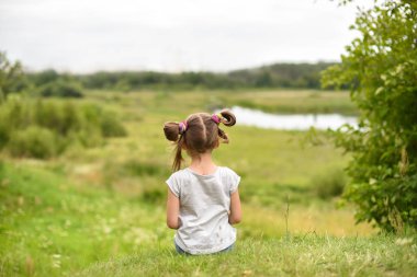 Yeşil bir topuk oturan küçük bir kız geri görüş ve onserving güzel bir manzara