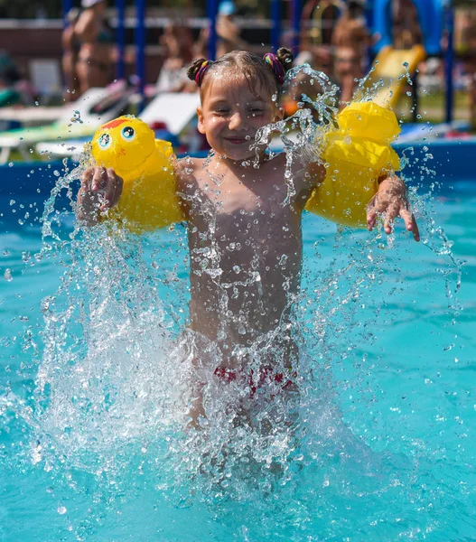 Una foto soleada de una niña sonriente disfrutando jugando y nadando en la piscina abierta — Foto de Stock