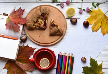 Bir fincan çay, elmalı turta, renkli yaprakları, açık bir dizüstü bilgisayar, bir çizim ve iyi bilenmiş kalem kümesi ile bir fotoğraf