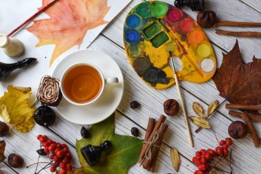Bir fincan çay, suluboya, bir çizim, bir kitap, sonbahar yaprakları ve tarçın ile rahat bir fotoğraf